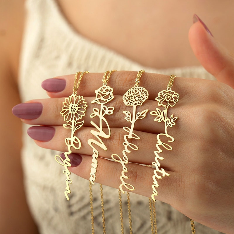 Four Birth Flower Name Necklaces close-up on model's manicured hand.